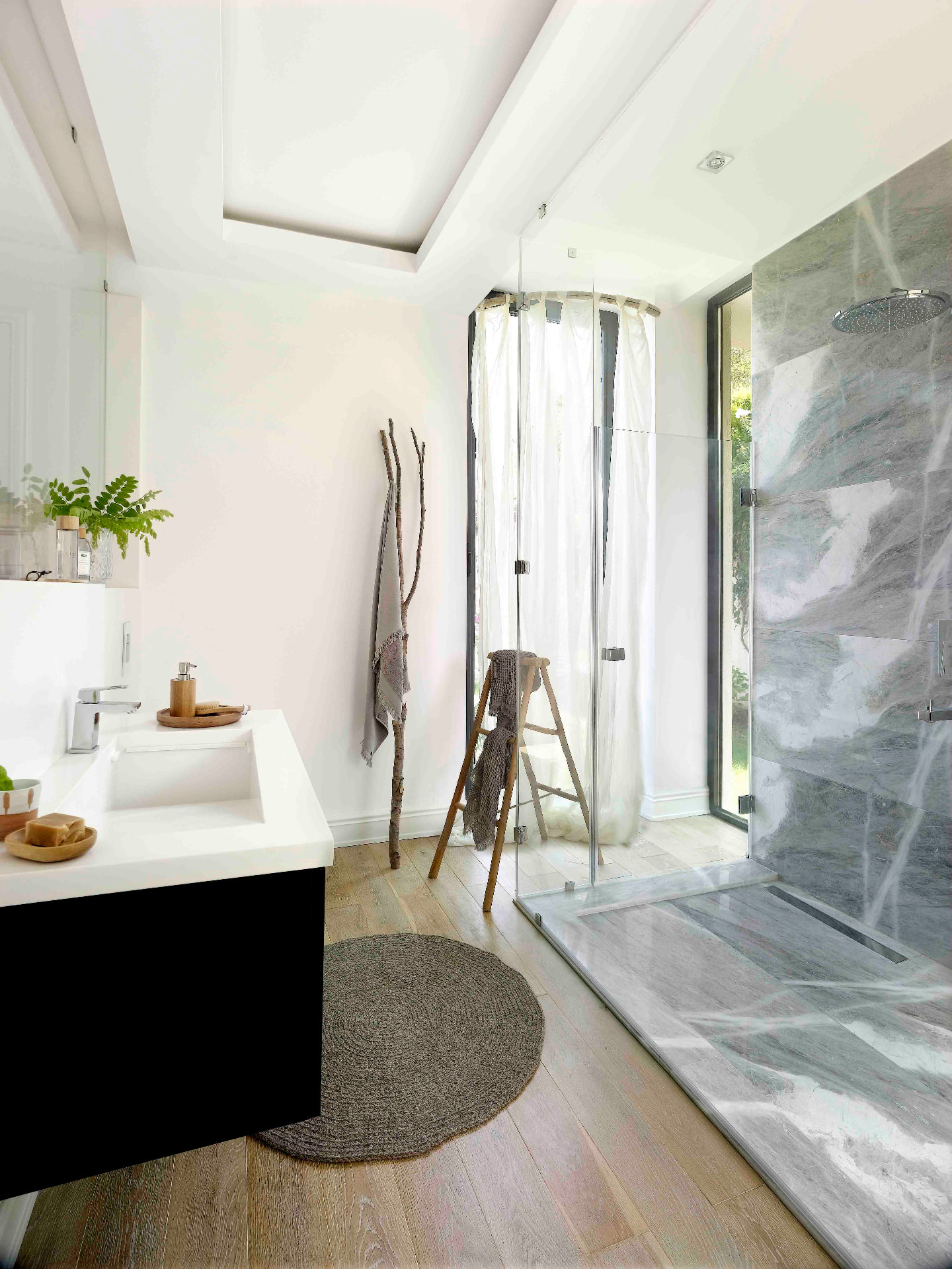 Another of the villa's bathrooms, with a grey marble rain shower, white vanity and full-height glass onto the garden