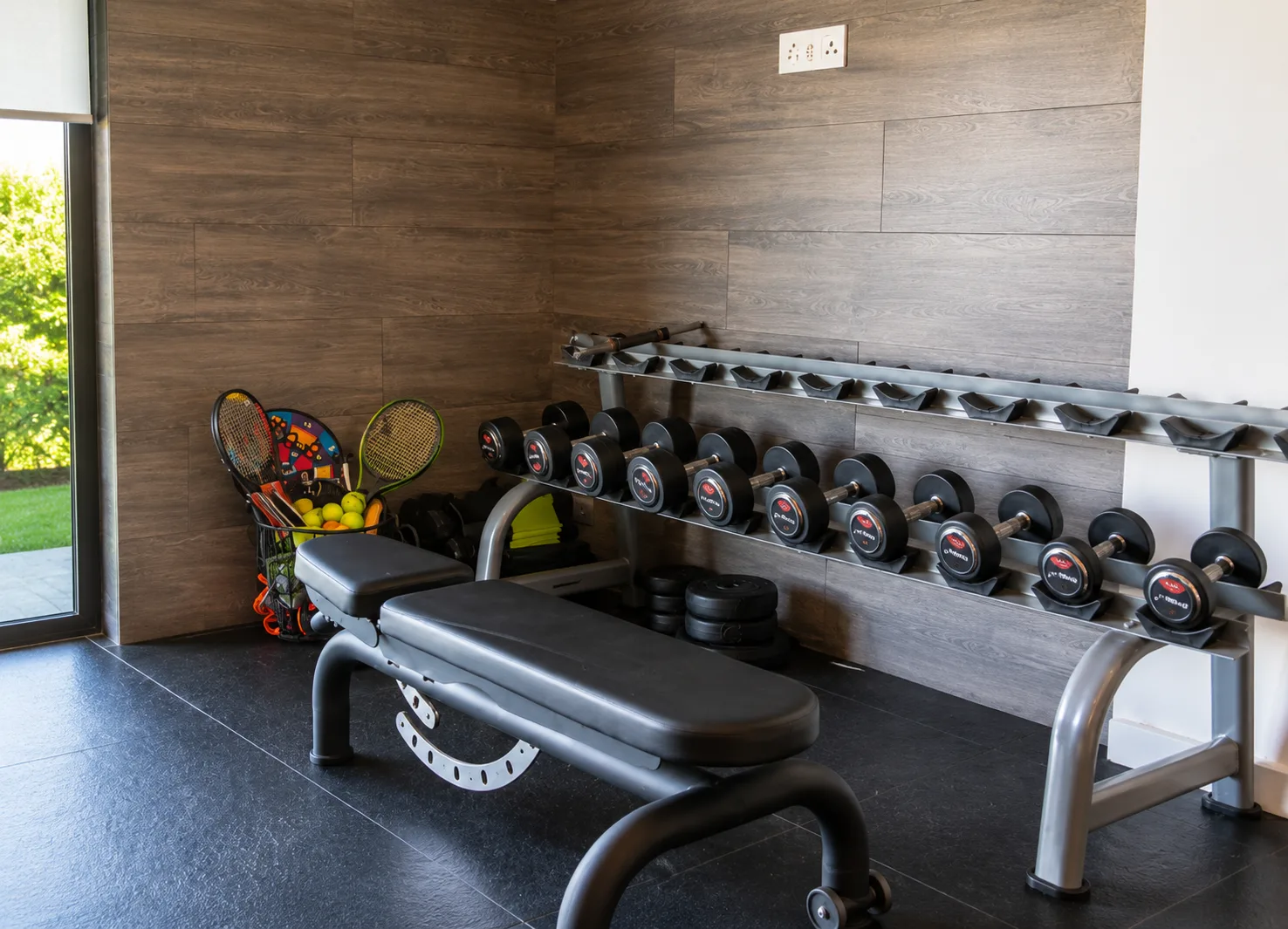 The villa's private gym, with a dumbbell rack, weights bench and full-height glass onto the garden