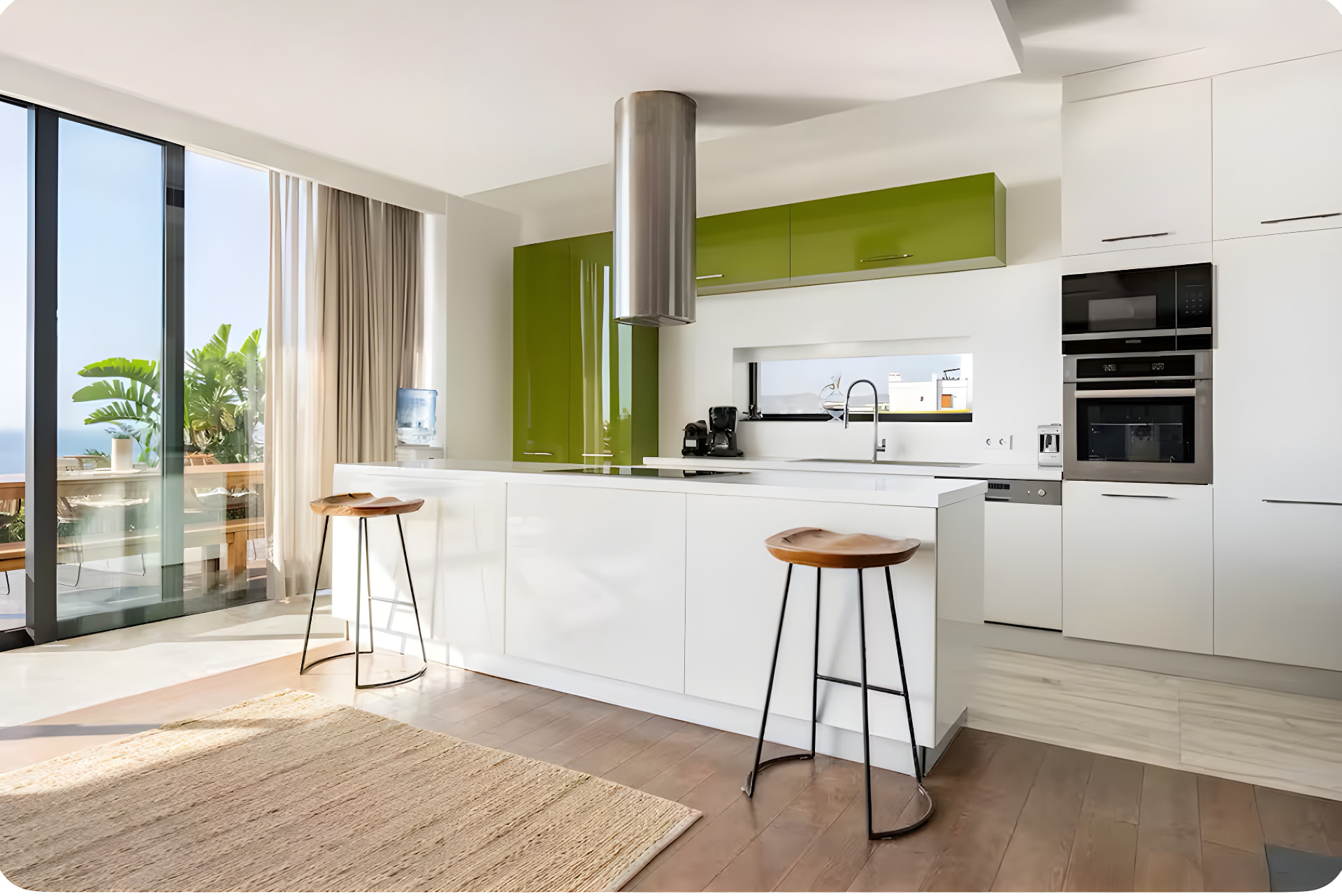 The villa's kitchen, with a white island counter, wooden bar stools, olive-green cabinetry and glass onto the sea