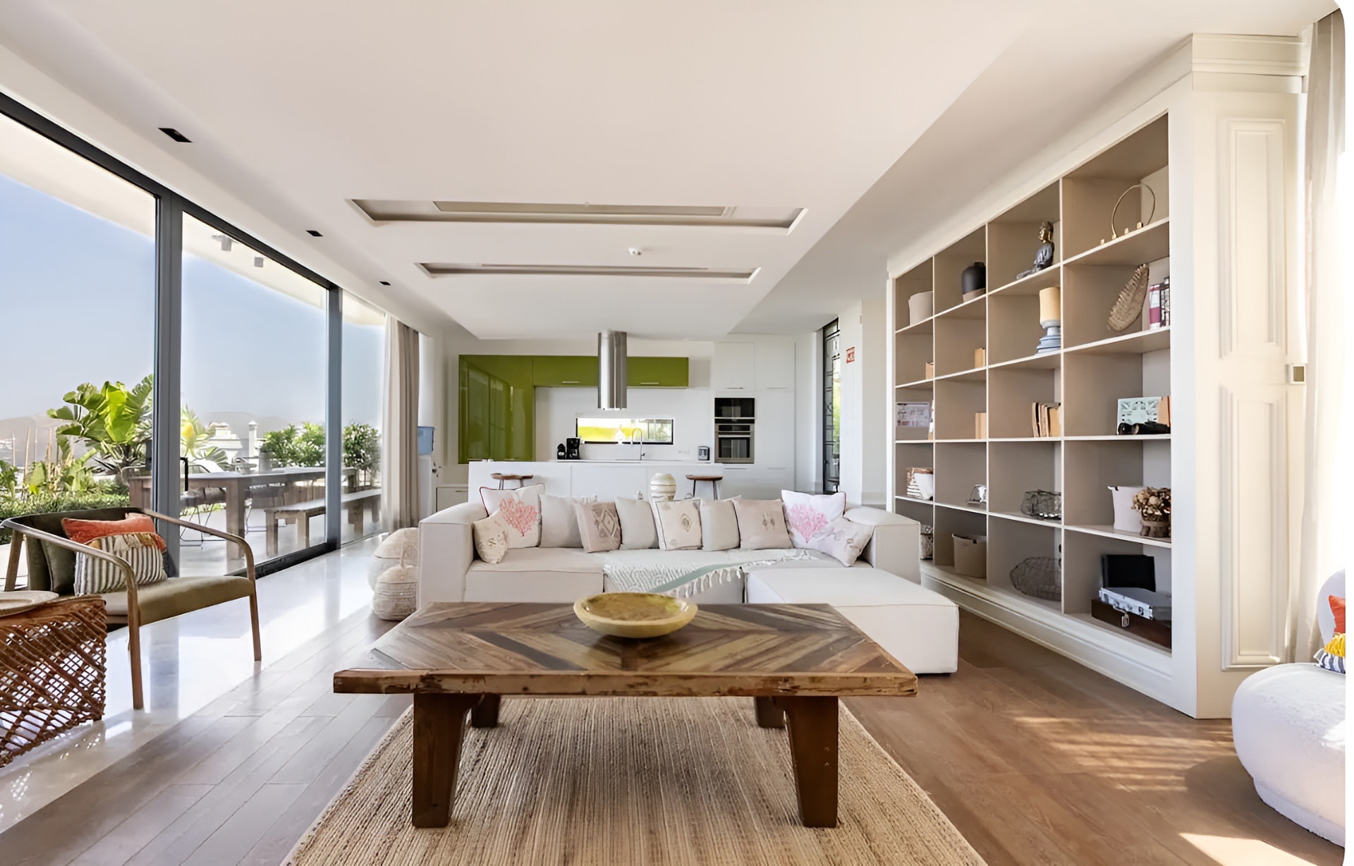 The villa's open-plan living space, with high ceilings, sliding glass onto the terrace, the kitchen beyond and a full-wall shelving unit