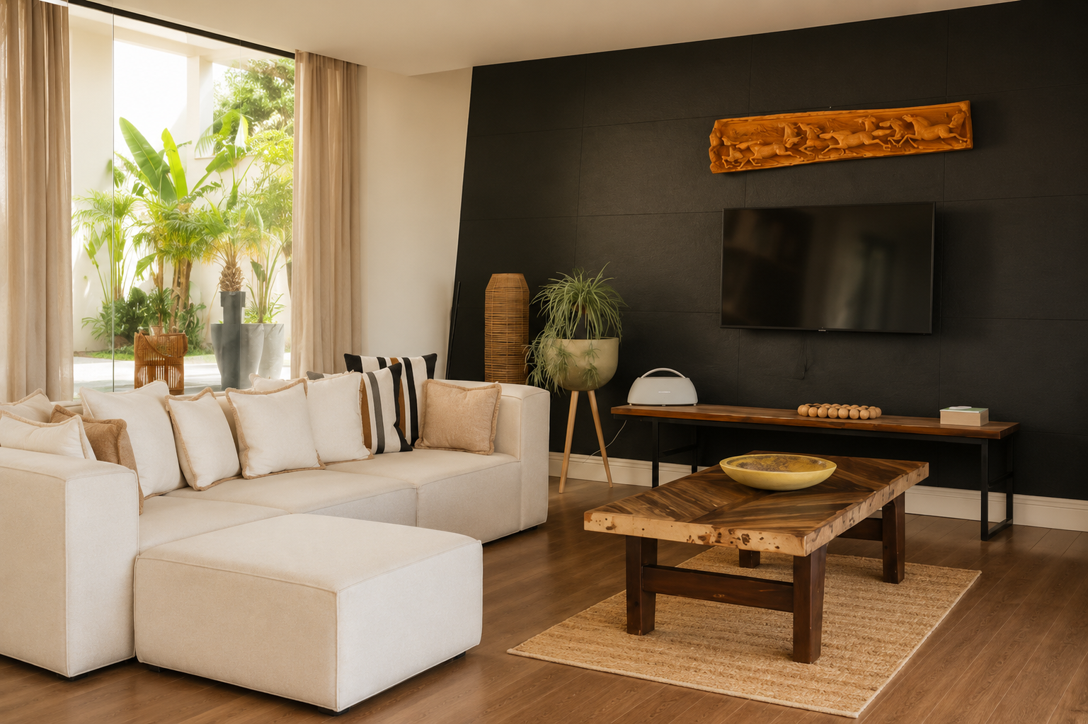 The villa's second lounge, with a cream modular sofa, live-edge wood table, carved wooden panel on the dark wall and glass onto the garden