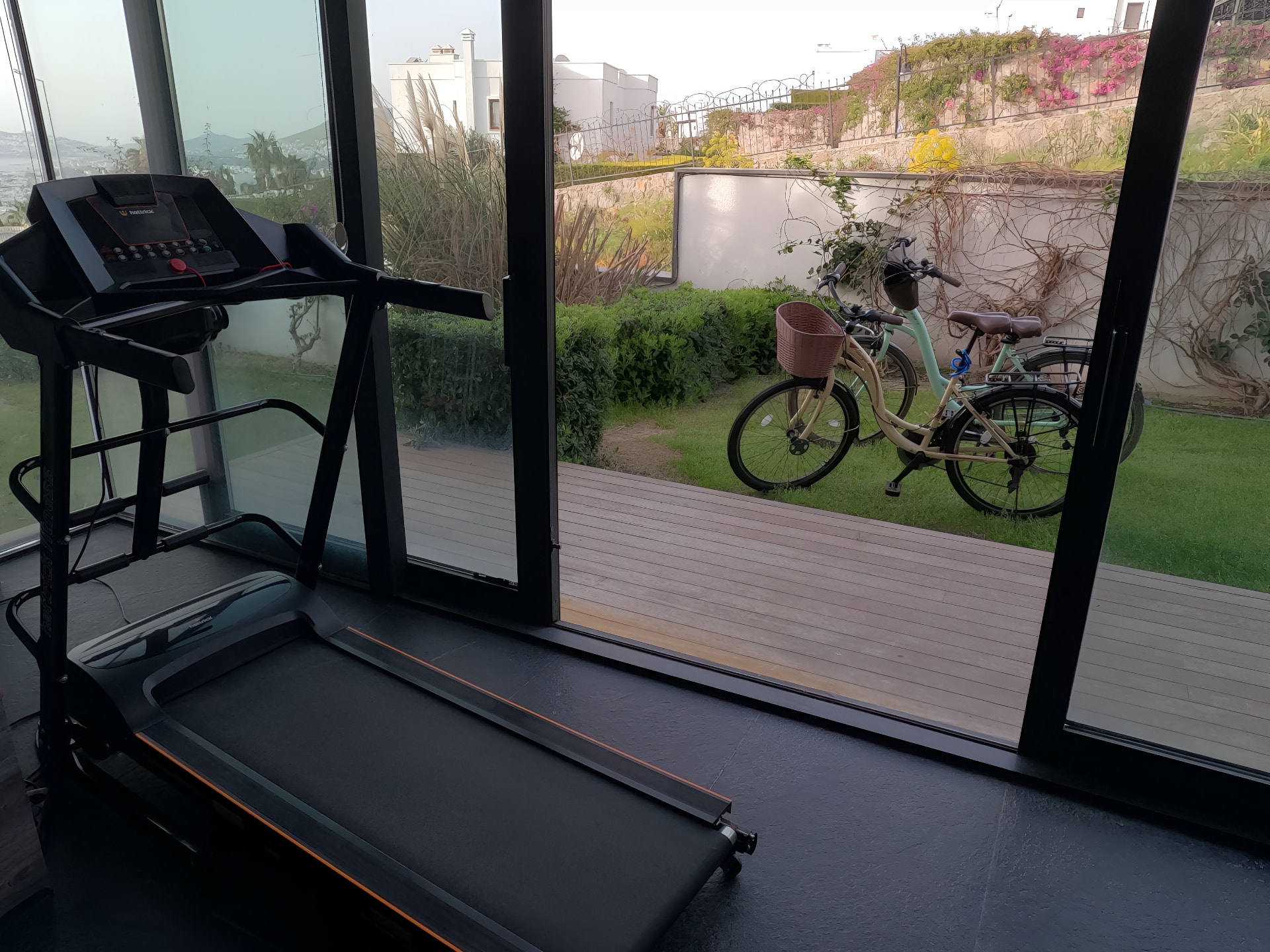 The villa's exercise space, with a treadmill facing full-height glass onto the garden and the bay, and the villa's bicycles outside