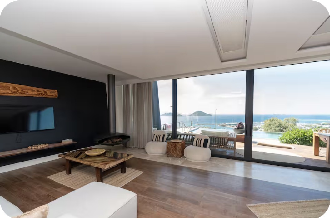 A modern villa living room with floor-to-ceiling glass doors opening to a terrace and the Aegean sea
