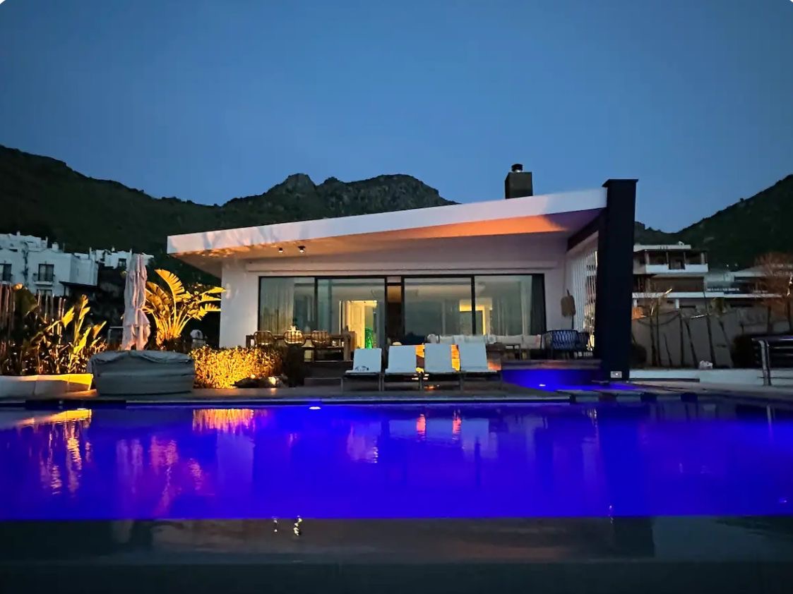 The villa in the evening, with the lit infinity pool, terrace loungers and the Bodrum hills behind
